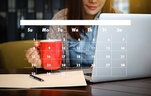 woman sitting at laptop with coffee cup. Image of monthly calendar.